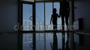 <strong>一个</strong>女人带着<strong>一个小</strong>女儿穿过酒店的<strong>玻璃</strong>门到长廊，美丽的海景。